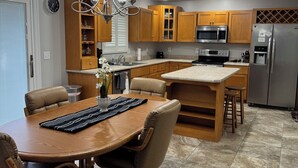 A modern kitchen with wooden cabinets, a central island, stainless steel appliances, and a dining area with a round table and chairs.