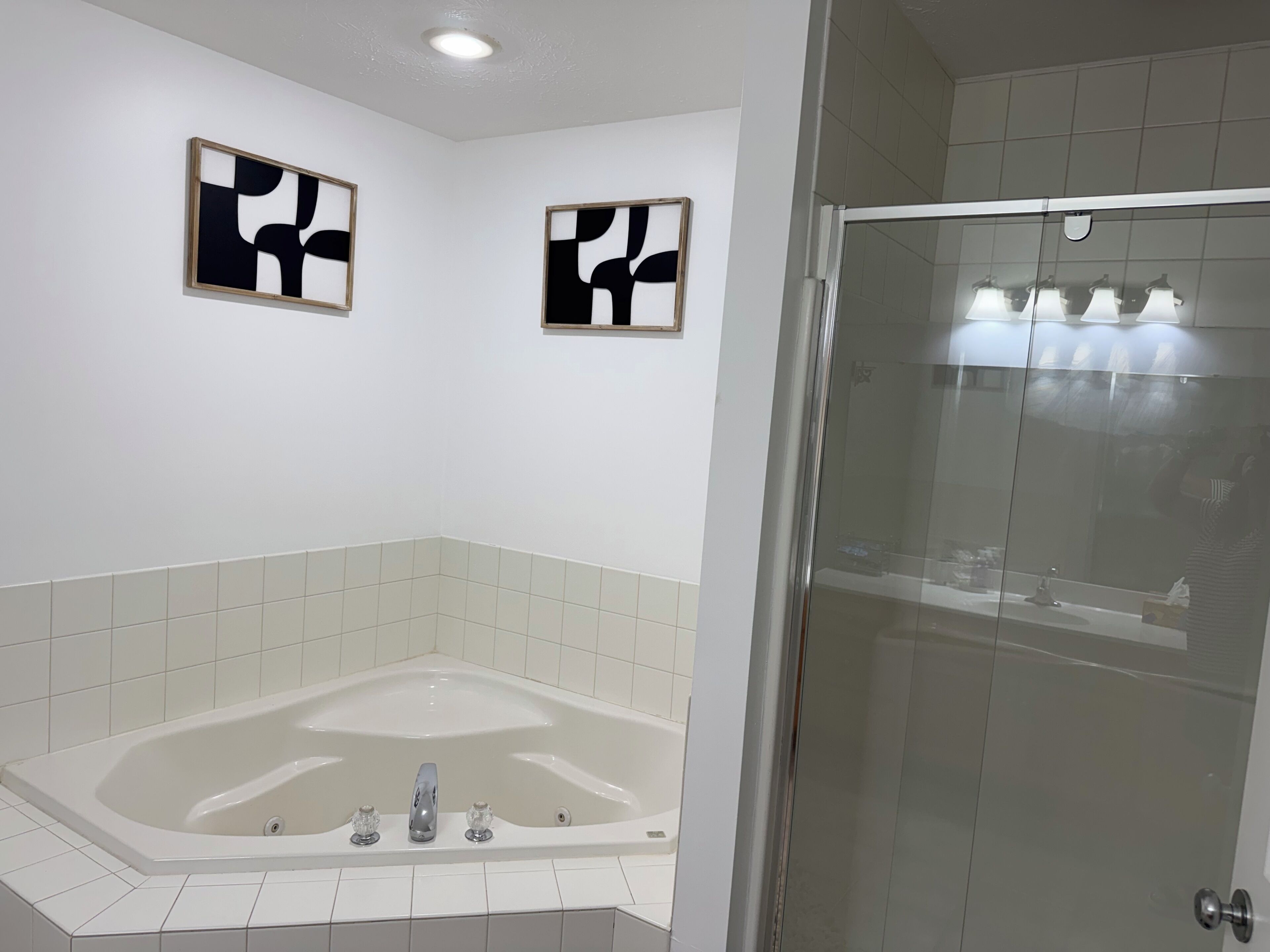 Une salle de bain moderne avec une baignoire sur pieds, une douche en verre et deux œuvres d’art abstraites accrochées au mur.