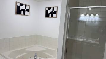 Une salle de bain moderne avec une baignoire sur pieds, une douche en verre et deux œuvres d’art abstraites accrochées au mur.