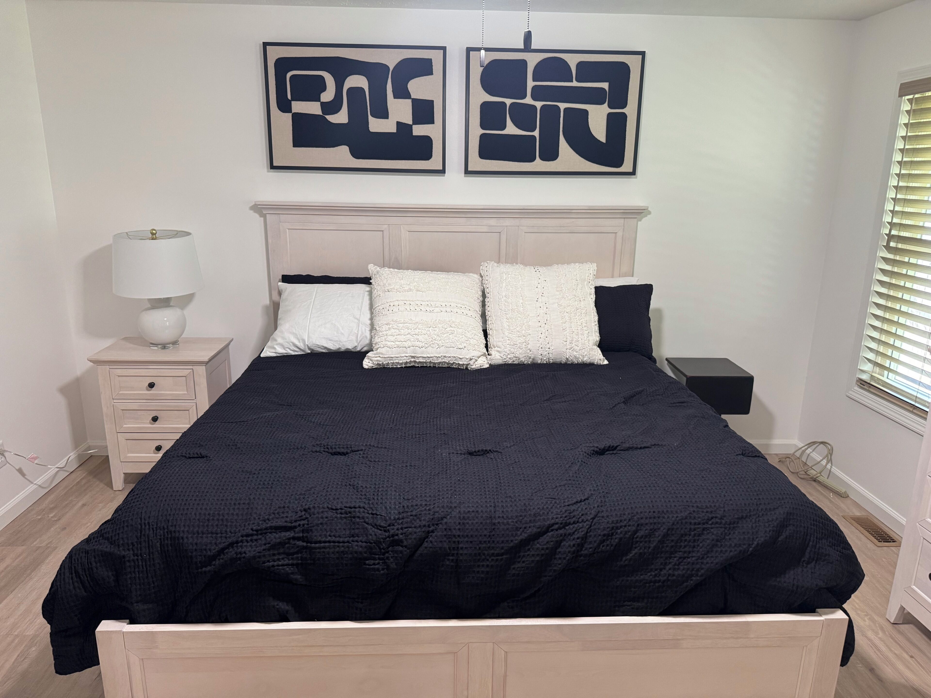 A bedroom with a bed, bedside tables, a lamp, and artwork on the wall.