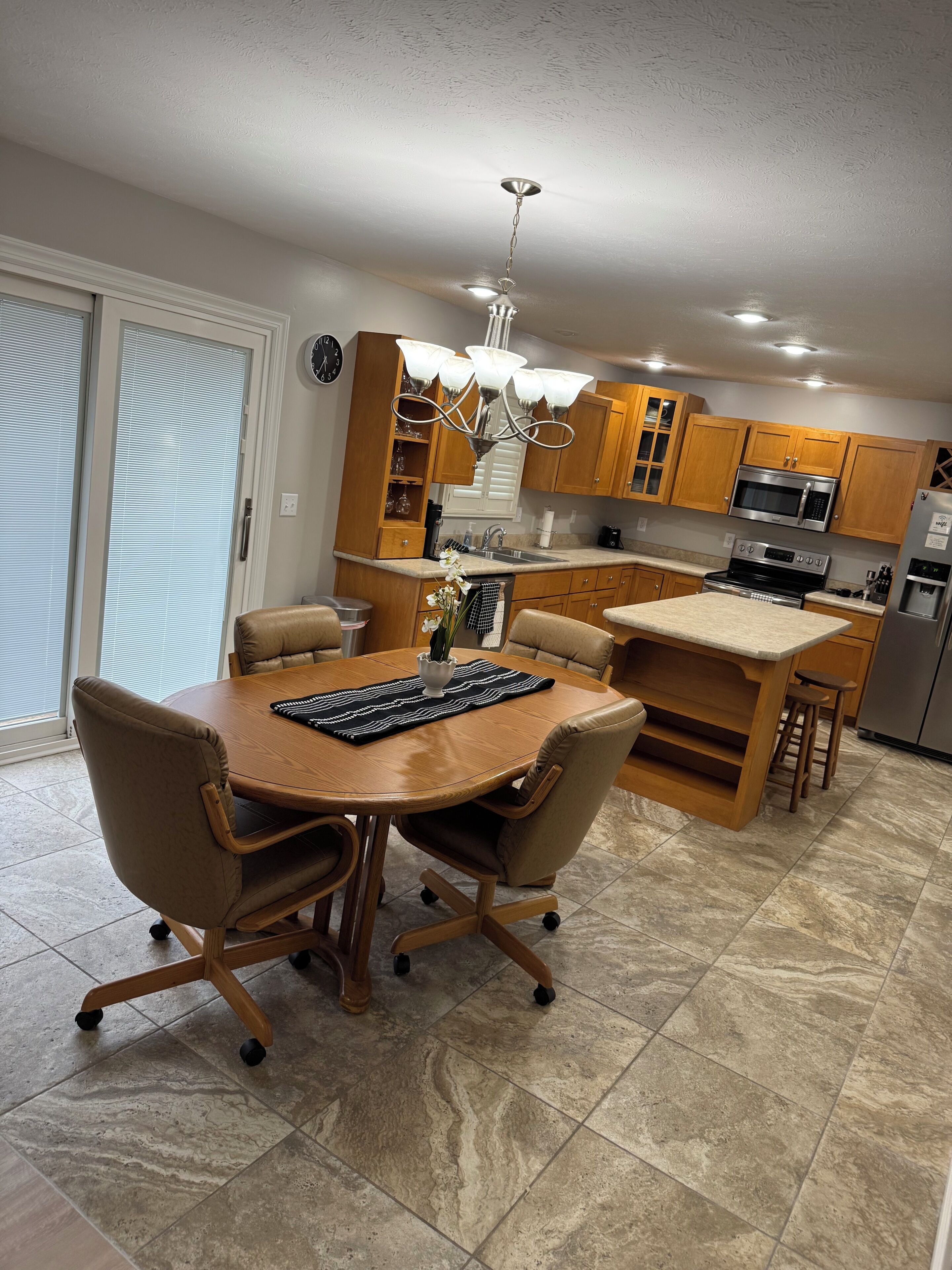 A modern kitchen with wooden cabinets, a stainless steel refrigerator, and a dining area with a round table and chairs.