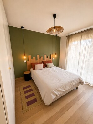 Quarto com cama, mesa de cabeceira, abajur e janela com cortinas.