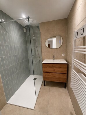 Une salle de bain moderne dotée d’une douche à parois de verre, d’un meuble-lavabo en bois et d’un porte-serviettes intégré.