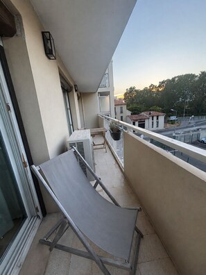 Varanda com mesa e cadeiras, um vaso de planta e vista para a rua e edifícios.
