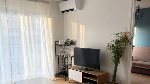 A modern living room with a flat-screen TV, a white coffee table, a sofa, a potted plant, and a glass display unit. - Cozy, air-conditioned 2-bedroom apartment, Toulon (Toulon)