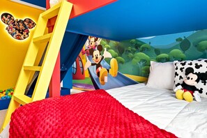Une chambre d’enfant avec un lit, une échelle, une fresque murale et un coussin à l’effigie de Mickey Mouse.