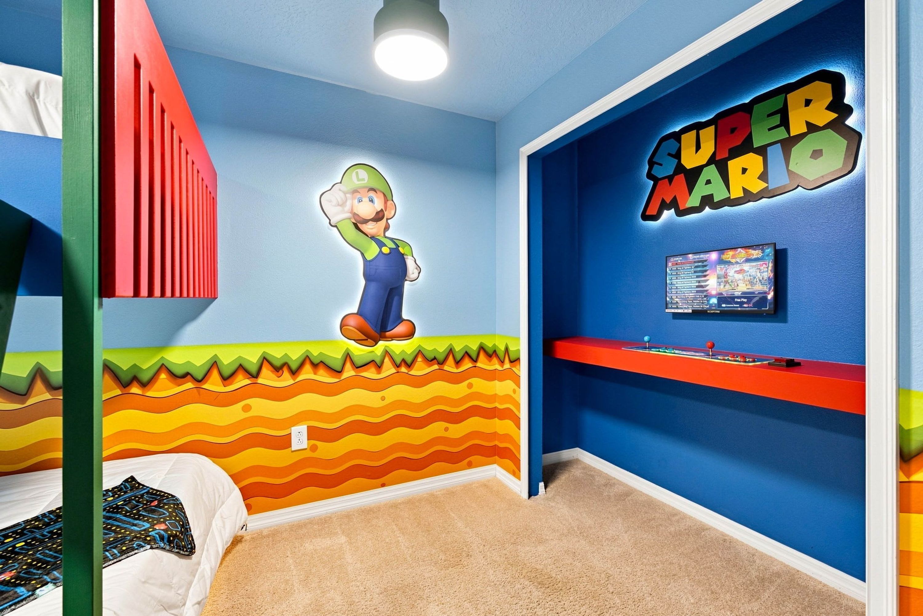 Une chambre avec un lit, une fresque murale représentant un personnage de jeu vidéo, une étagère avec une console de jeu et un décor mural coloré.