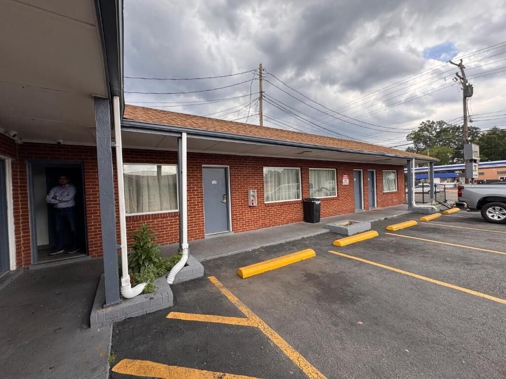Een motel met een overdekte veranda, een parkeerplaats met aangegeven parkeerplaatsen, en een gevel van baksteen.