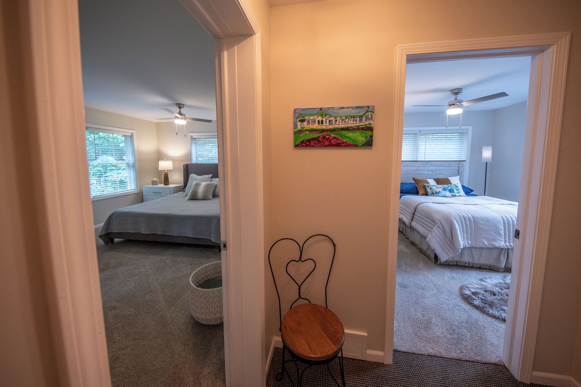 A hallway leading to two bedrooms with ceiling fans, a painting on the wall, and a pet bed.
