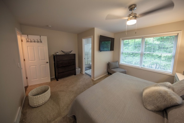 A bedroom with a bed, a dresser, a window with blinds, a ceiling fan, and a door.