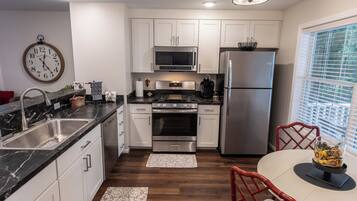 A modern kitchen with white cabinets, stainless steel appliances, a marble countertop, and a dining area with a red chair.