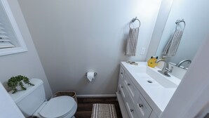 Un bany amb un vàter blanc, un lavabo amb un mirall i una planta petita a l'esquerra.