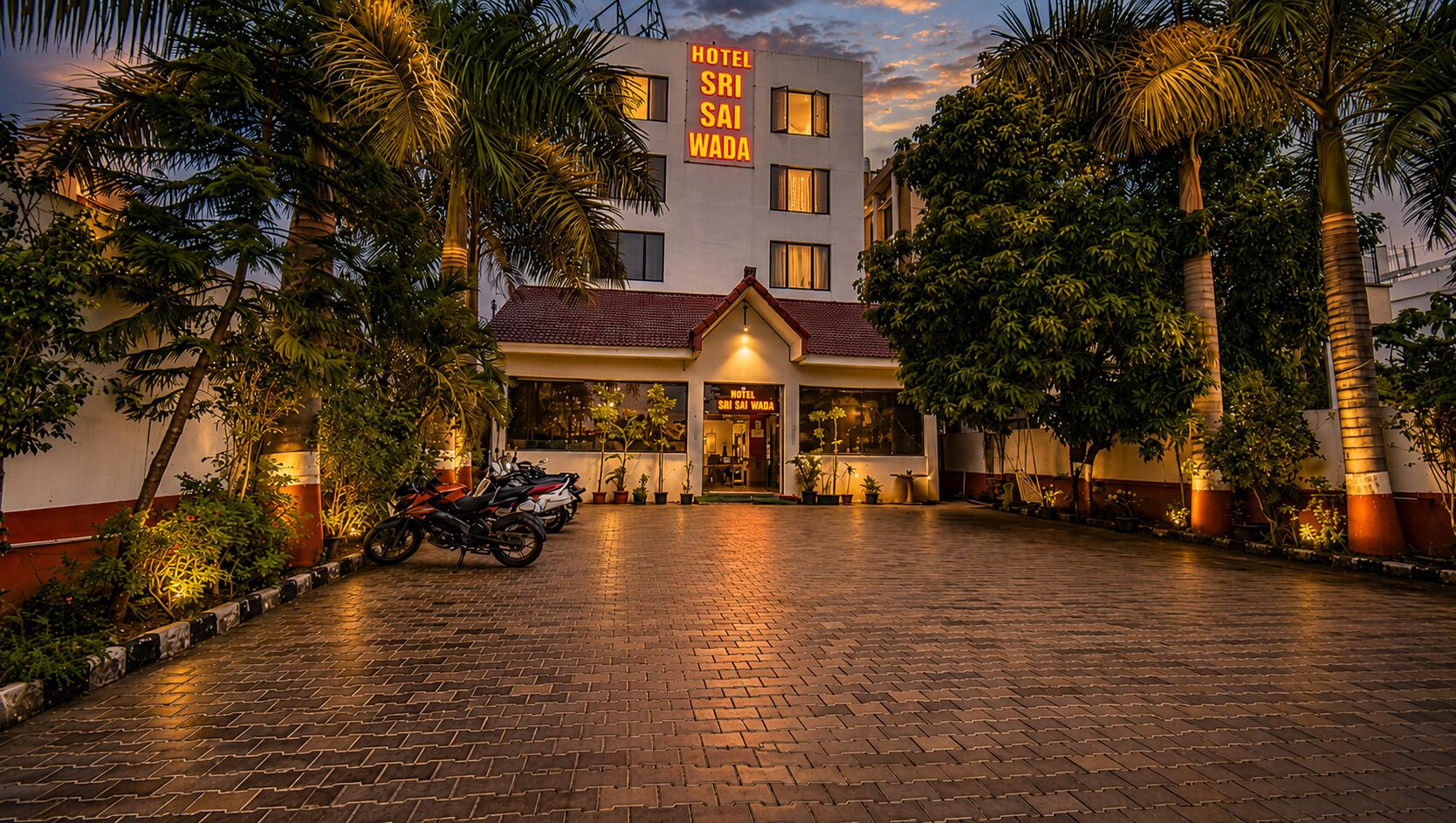 A hotel with a paved entrance, a signboard, and a row of parked motorcycles.