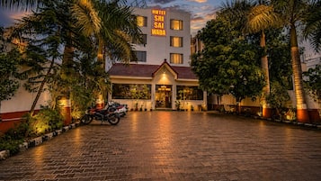 A hotel with a paved entrance, a signboard, and a row of parked motorcycles.