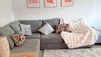 A modern living room with a grey sectional sofa, decorative pillows, a white furry throw blanket, and three framed artworks on the wall.