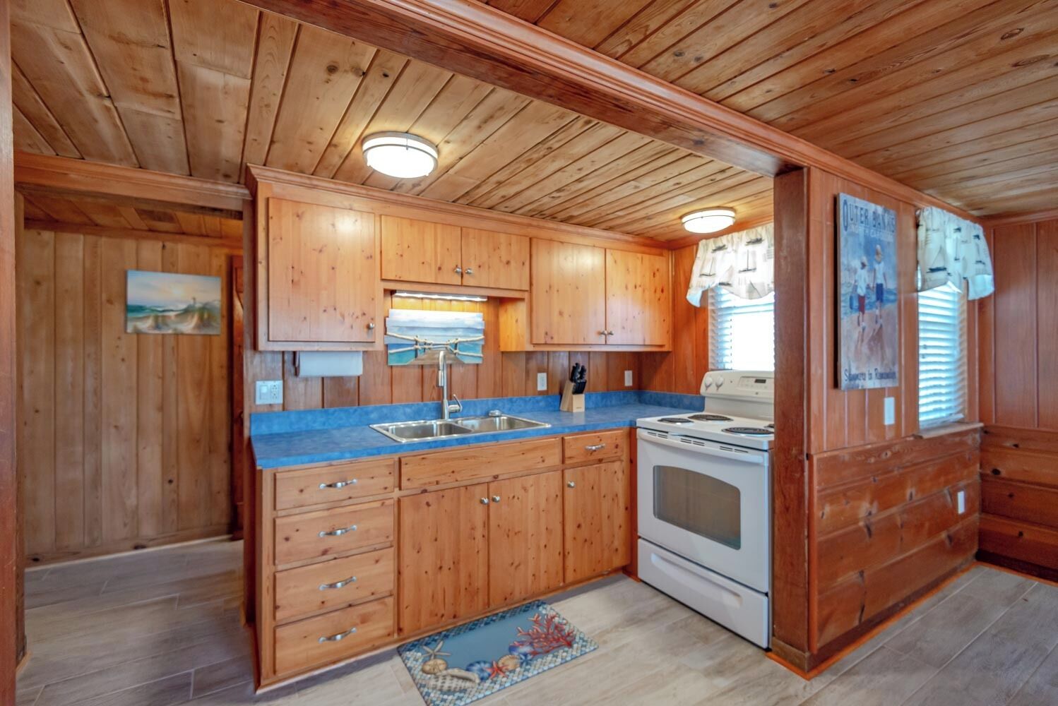 A wooden cabin interior with a kitchen area including a stove, sink, and cabinets.
