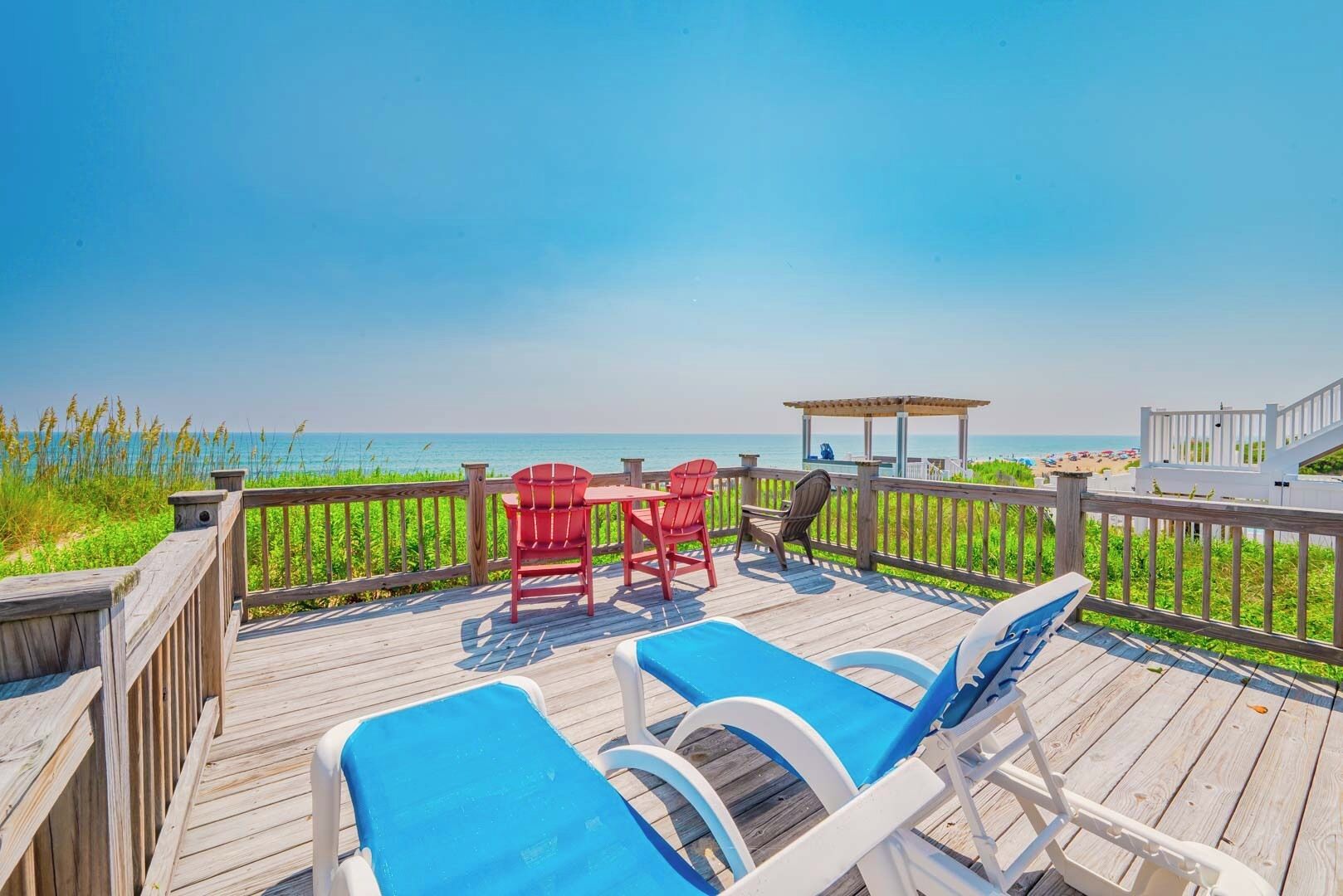 A wooden deck with lounge chairs and a table, overlooking a beach.