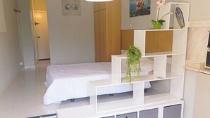 Et soveværelse med seng, et hvidt skrivebord, en stol og en hængende lampe.