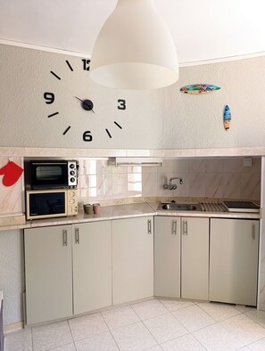 A kitchen with a clock, microwave, oven, sink, and cabinets. - Your corner by the sea (Vila-seca)