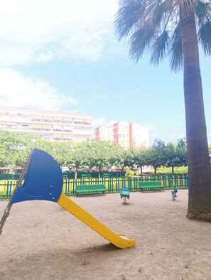 A playground with a seesaw, sand, benches, and a palm tree. - Your corner by the sea (Vila-seca)