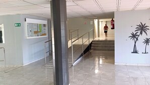 En rummelig lobby med flisegulv, en central søjle, trappe og en væg med et tropisk muralmaleri.