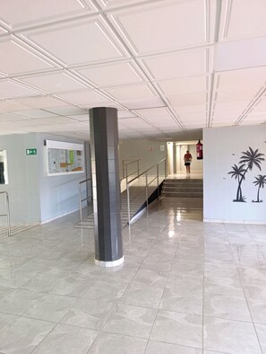 Eine geräumige Lobby mit gefliestem Boden, einer zentralen Säule, einer Treppe und einer Wand mit einem tropischen Wandgemälde.