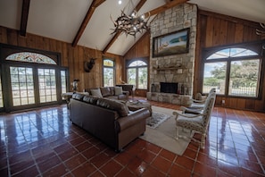 A spacious living room with a stone fireplace, leather furniture, and large windows.