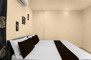 Une chambre d’hôtel avec un lit, un climatiseur fixé au mur et trois tableaux encadrés.