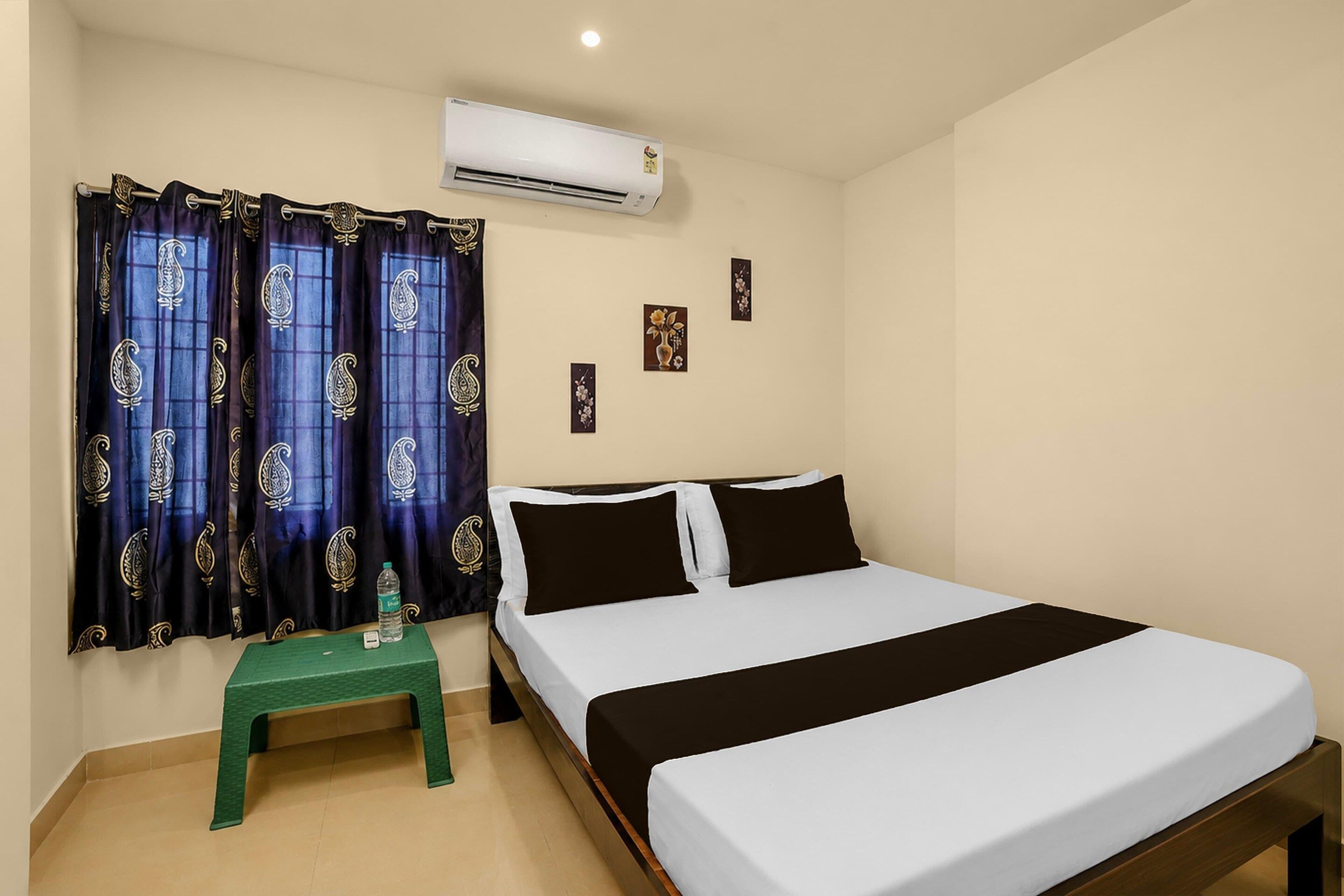 A hotel room with a bed, a small table, and an air conditioning unit.