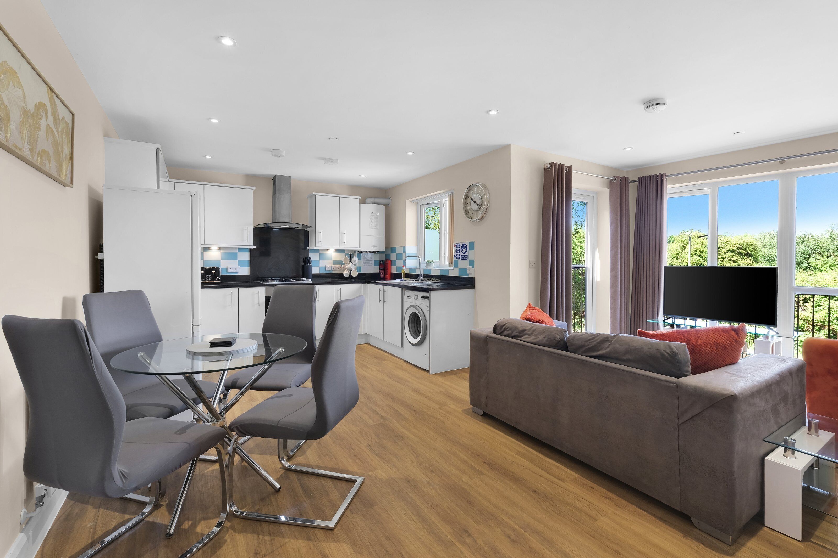 A modern apartment with a dining area, kitchen, living room, and a balcony with a TV.