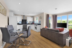 A modern apartment with a dining area, kitchen, living room, and a balcony with a TV. - Heathrow Living 2BDR 2BA Apt 06-360stays (Stanwell)