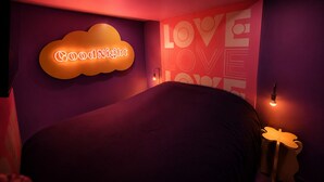 Ein Zimmer mit einem Bett, einem Neon-Schild mit der Aufschrift 'Good Night' und einer Wand, auf der 'LOVE' in großen Buchstaben steht.