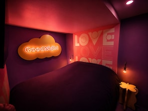 Ein Zimmer mit einem Bett, einem Neon-Schild mit der Aufschrift 'Good Night' und einer Wand, auf der 'LOVE' in großen Buchstaben steht.