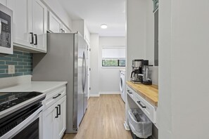 A compact kitchen with white cabinets, a stainless steel refrigerator, a coffee maker, and a washing machine. - Remodel Condo overlooks Pool walk to Celebration Park Beach & Coligny! (Hilton Head Island)