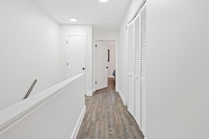Un estrecho pasillo con paredes blancas y suelo de madera, que conduce a una habitación con una puerta y una ventana.