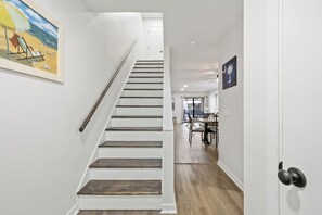 Una escalera de madera con barandilla metálica que conduce a un comedor con mesa y sillas.