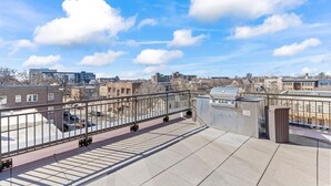 Eine Dachterrasse mit Metallgeländer, einem Grill und Blick auf die Stadt.