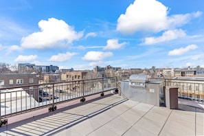 Eine Dachterrasse mit Metallgeländer, einem Grill und Blick auf die Stadt.