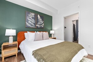 Ein Schlafzimmer mit einem Bett, zwei Nachttischen mit Lampen, einer grünen Wand und einer Tür zu einem anderen Raum.