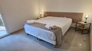 Ein modernes Schlafzimmer mit einem großen Bett, zwei Nachttischen mit Lampen und Blick durch eine Glastür.