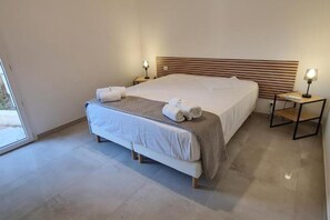 Ein modernes Schlafzimmer mit einem großen Bett, zwei Nachttischen mit Lampen und Blick durch eine Glastür.