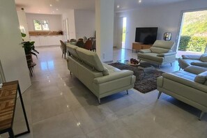Ein geräumiges Wohnzimmer mit einer Sofagarnitur, einem Flachbildfernseher und einem Essbereich im Hintergrund.