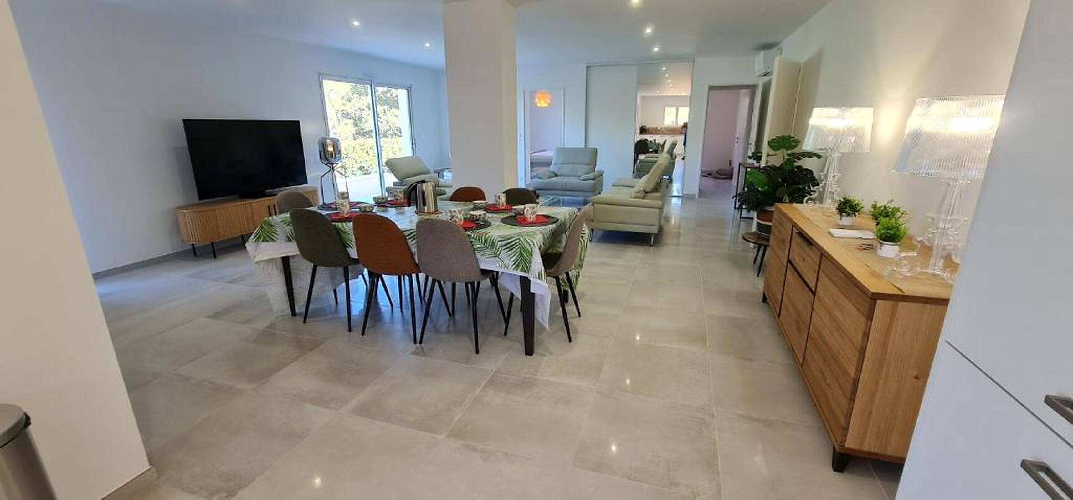 A spacious living area with a dining table set for four, a sofa, and a TV.