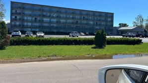 Un immeuble à plusieurs étages doté de balcons, un parking avec plusieurs voitures et une zone herbeuse avec un petit étang.