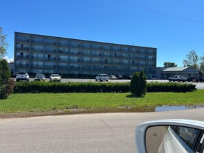 En byggnad med flera våningar och balkonger, en parkeringsplats med flera bilar och ett grönområde med en liten damm.