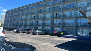 A multi-story hotel with balconies, a parking lot, and a building entrance.