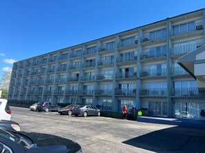 A multi-story hotel with balconies, a parking lot, and a building entrance.