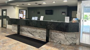 A reception desk with a marble counter, a black mat, and a glass door leading outside.