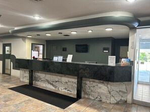 A reception desk with a marble counter, a black mat, and a glass door leading outside.