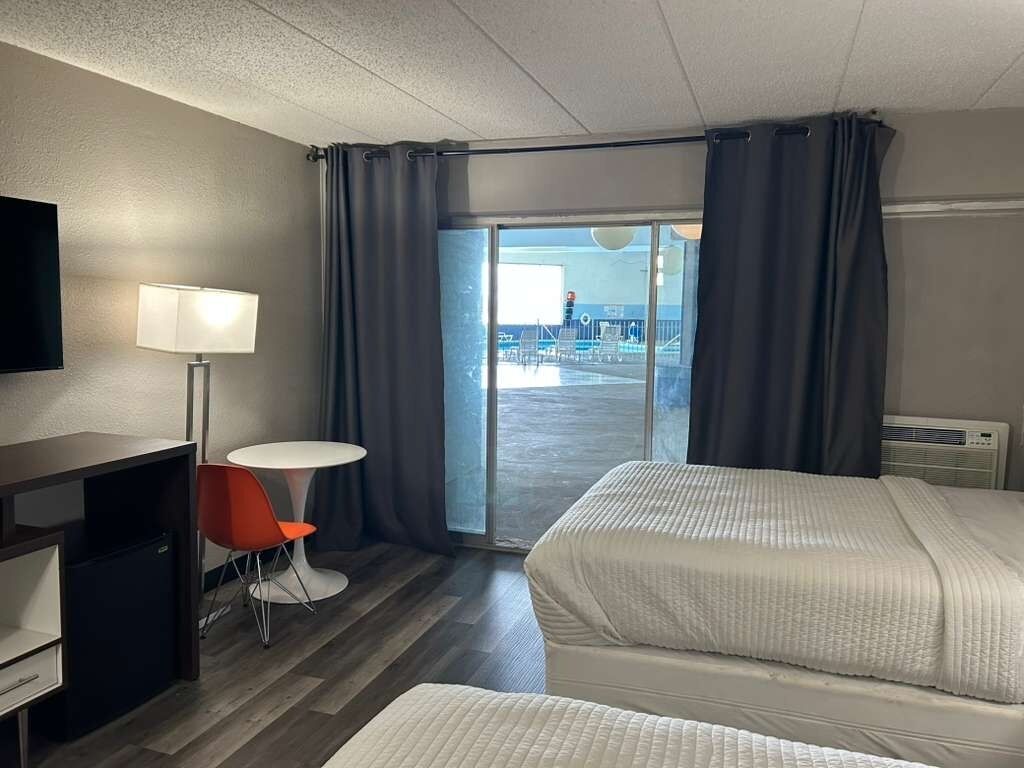 Une chambre d’hôtel avec deux lits, un bureau, une chaise, une télévision et une vue sur la piscine.